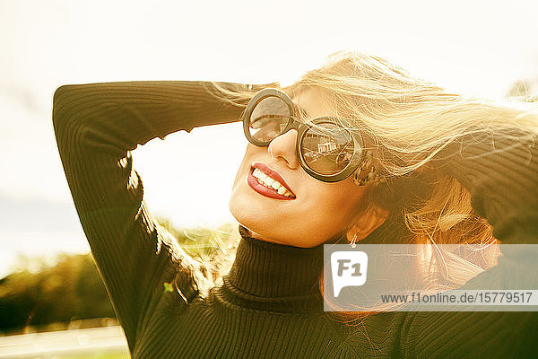 Porträt einer blonden Frau mit Sonnenbrille und lächelnden Händen im Haar