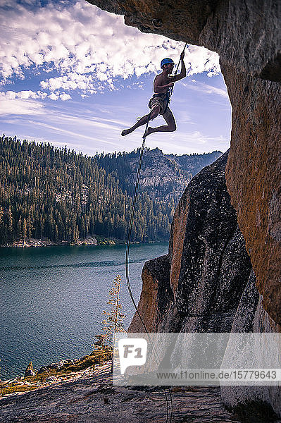 Young male rock climber dangling on rope from rock face High Sierras California USA
