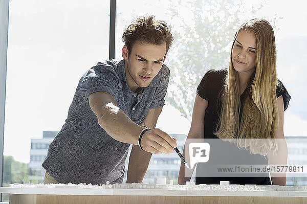 Zwei junge Architekten stehen an einem Tisch und arbeiten an einem Architekturmodell.