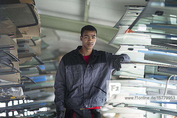 Workman leaning against stack of car windshield in workshop