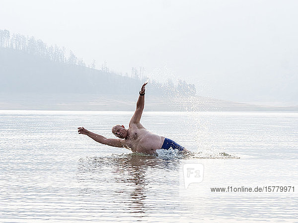 A senior man splashing and swimming in lake water  a heavy haze in the air  smoke effect of bush fires.