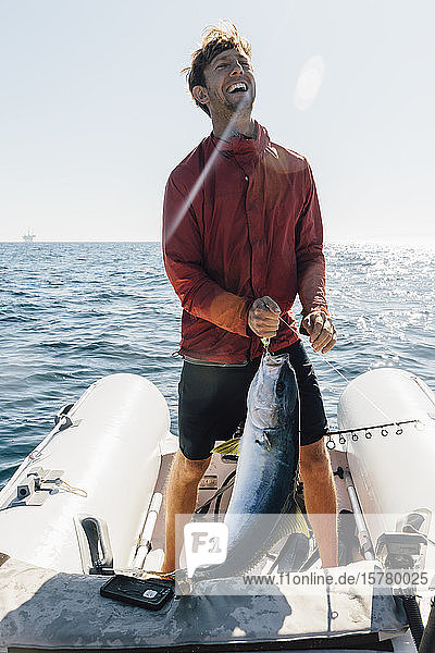 Man standing on inflatable dinghy holding freshly caught fish.