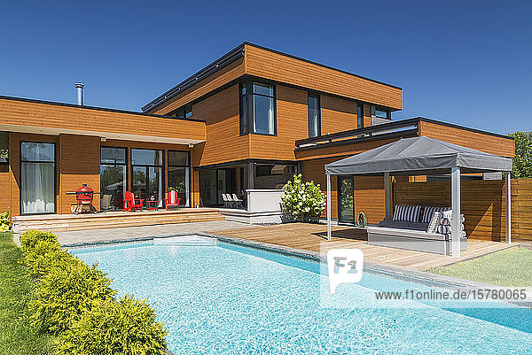 Exterior view of modern cube style home with stained horizontal wood cladding swimming pool and wooden deck with gazebo canopy Quebec Canada.