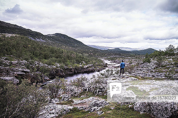 Mann steht über einem Flussufer mit Bergen  Lakselv  Norwegen