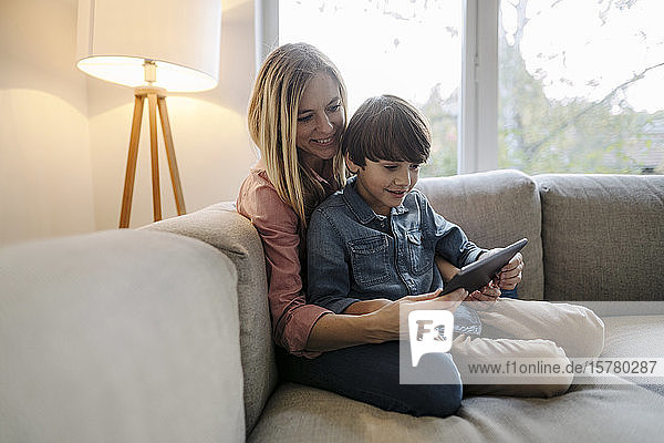 Mother and son sitting on couch  using digital tablet