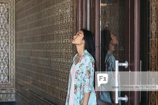 Porträt einer schönen jungen Frau  die einen Kimono trägt und sich reflektierend an eine Tür lehnt