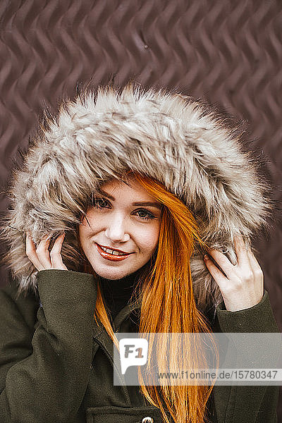 Porträt einer lächelnden rothaarigen jungen Frau mit Kapuzenjacke