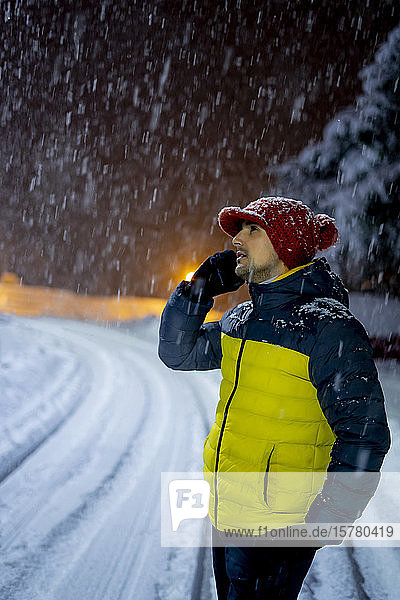 Mann am Telefon bei Schneefall in der Nacht