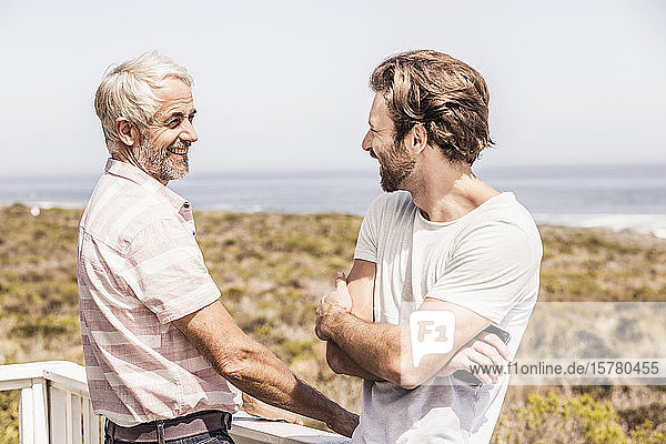 Vater und erwachsener Sohn unterhalten sich auf einer Terrasse am Meer