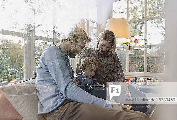 Little boy with parents unwrapping gift in sunroom at home