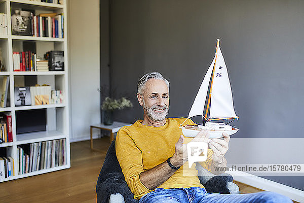 Smiling mature man at home holding model sailboat