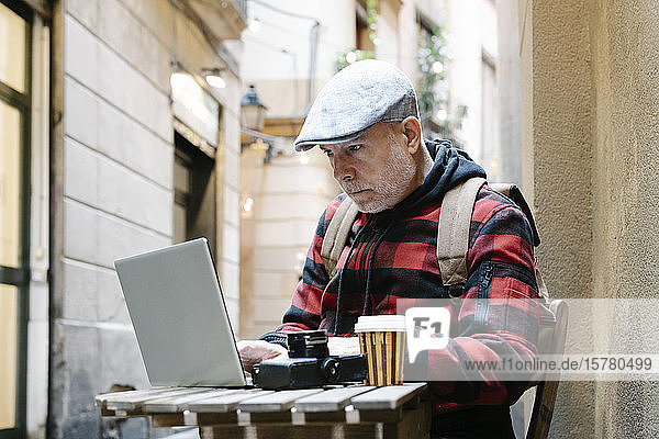 Porträt eines älteren Mannes  der mit einem Laptop in einem Straßencafé sitzt  Barcelona  Spanien