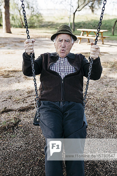 Old man swinging on playground in park