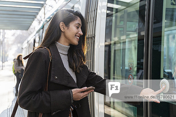 Lächelnde junge Frau drückt den Knopf an einer Straßenbahn