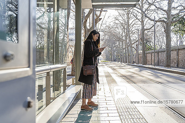 Young woman with smartphone waiting at the tram stop