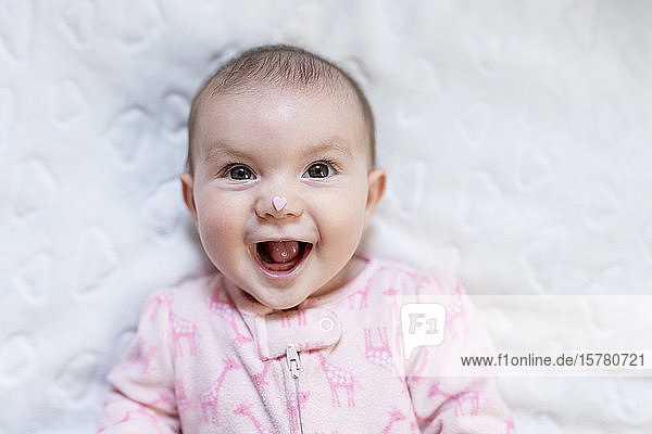 Porträt eines glücklichen kleinen Mädchens mit rosa herzförmigen Bonbons auf der Nase