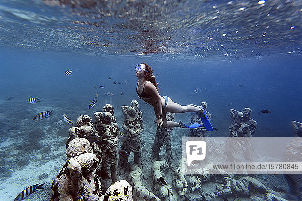 Woman swimming near underwater sculpture made by Jason deCaires Taylor Gili Meno island Bali Indonesia