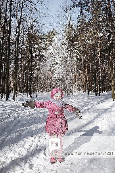Little girl throwing snow in winter forest