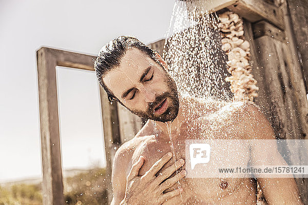 Junger Mann duscht in einer Außendusche