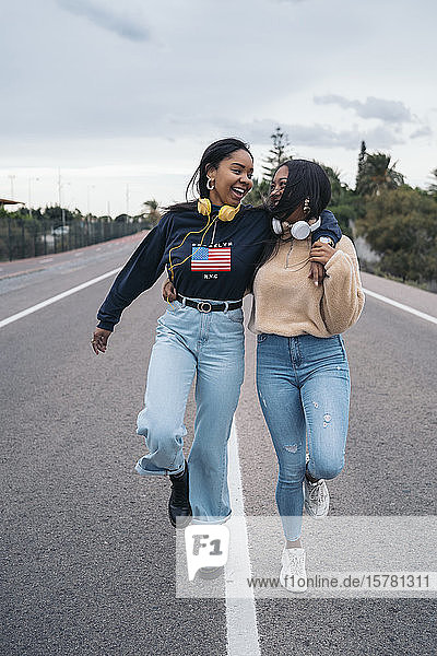 Two happy young women walking on a road