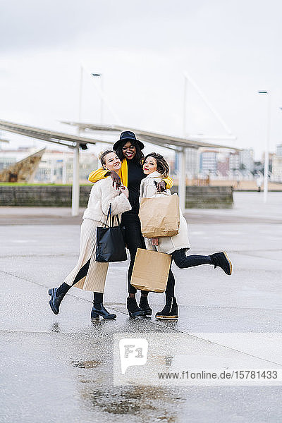 Porträt von glücklichen Freundinnen mit Einkaufstüten  die sich in der Stadt umarmen