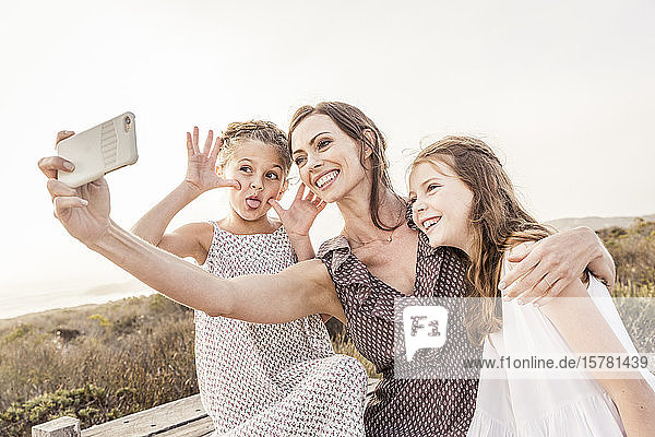 Happy mother taking a selfie with her two daughters on a boardwalk at sunset