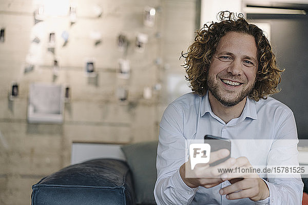 Portrait of happy businessman with cell phone having a break in office