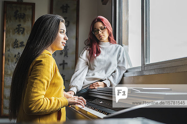 Teenage girl playing piano at home while her friend listening