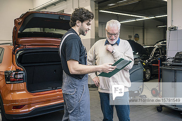 Car mechanic explaining ckeck list to client in workshop