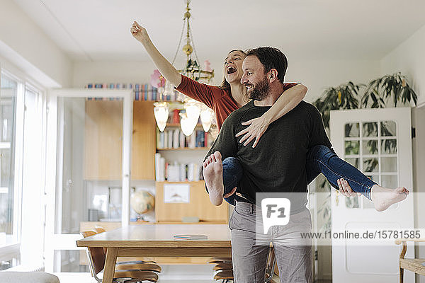Man carrying happy woman piggyback in their comfortable home
