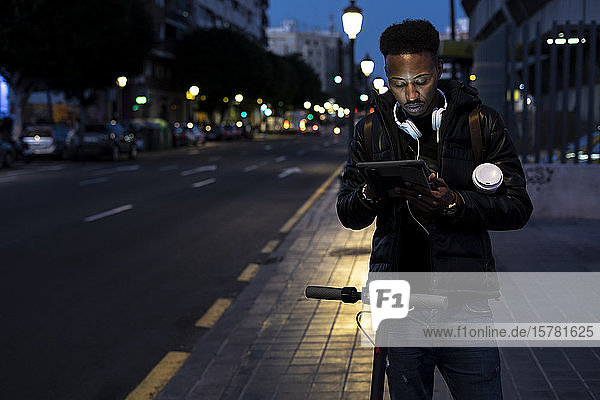 Man in the city at night with tablet and e-scooter