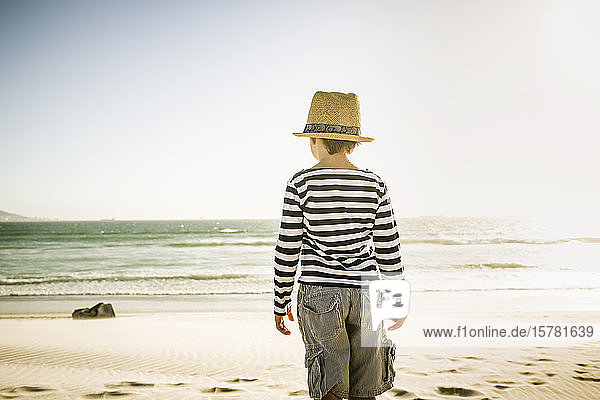 Rear view of boy with hat standing on the beach