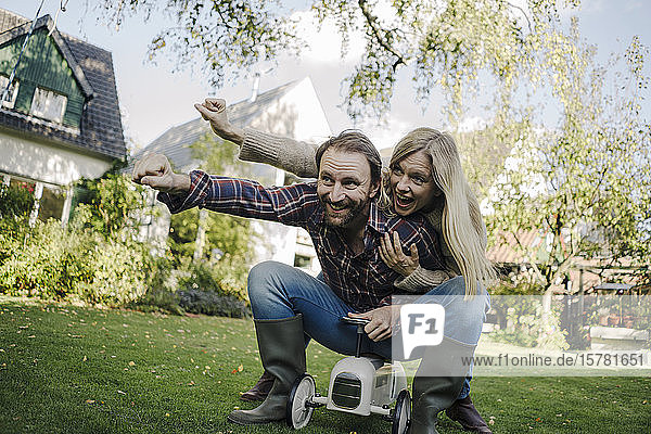 Lachendes Paar  das vorgibt  im Garten auf einem Spielzeugauto zu fliegen