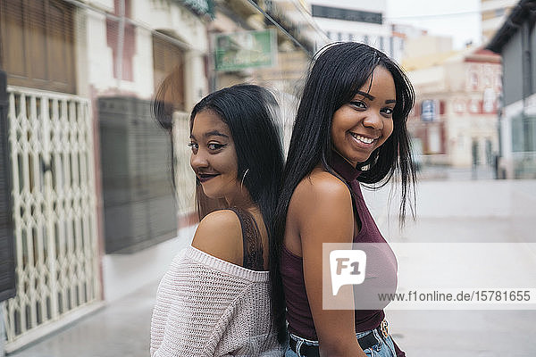 Porträt von zwei glücklichen jungen Frauen  die Rücken an Rücken in der Stadt stehen