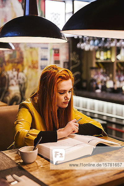 Redheaded young woman at table in a pub looking at a book