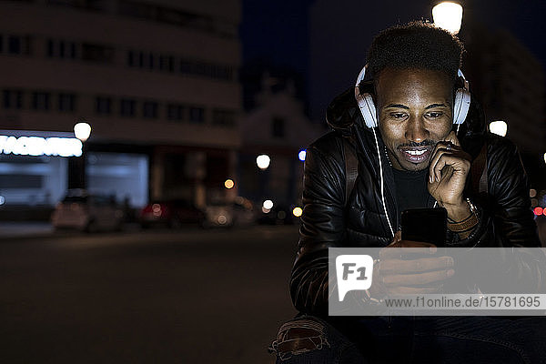 Man in the city at night with smartphone and headphones