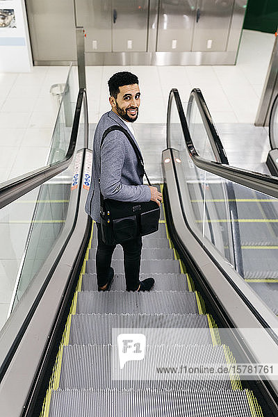 Porträt eines lächelnden jungen Geschäftsmannes auf einer sich umdrehenden Rolltreppe