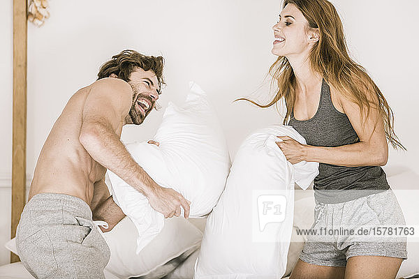 Sorgenfreies junges Paar bei einer Kissenschlacht im Bett