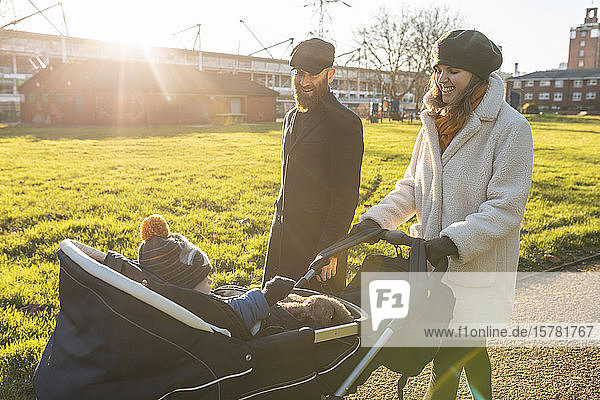Glückliches Paar mit kleinem Sohn in einem Kinderwagen im Park
