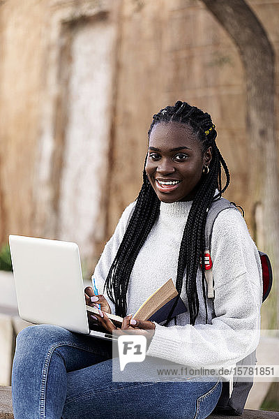 Porträt einer glücklichen Studentin  die auf einer Bank sitzt