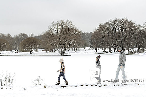 Vater und zwei Kinder spazieren in Winterlandschaft