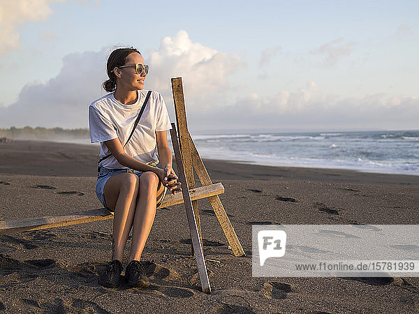 Frau sitzt in der Abenddämmerung auf einem Gestell am Strand  Strand von Kedungu  Bali  Indonesien
