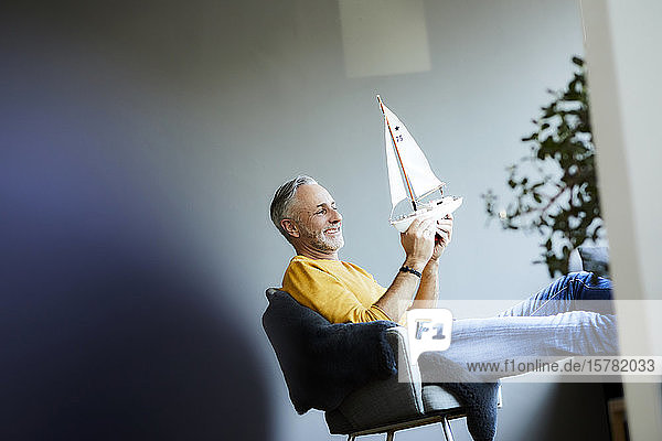 Smiling mature man at home holding model sailboat