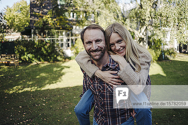 Man carrying happy woman piggyback in garden