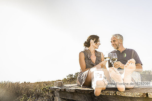 Glückliches Paar sitzt auf der Strandpromenade an der Küste und genießt ein Glas Weißwein