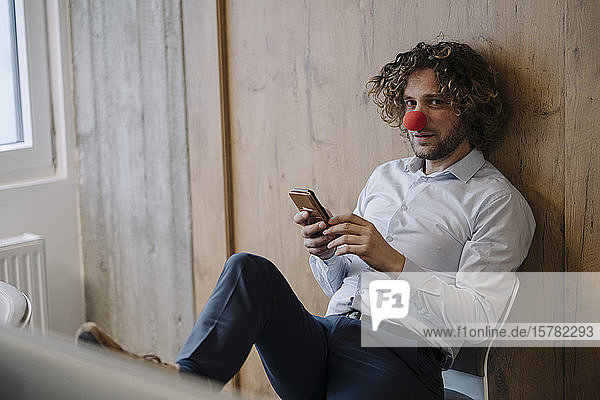Portrait of businessman with red clown nose using cell phone in office