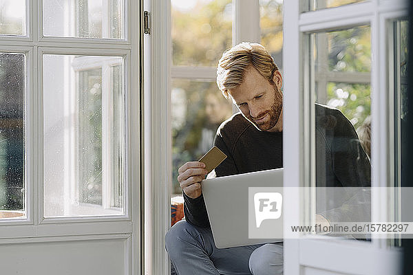 Mann benutzt Laptop und Kreditkarte im Wintergarten zu Hause