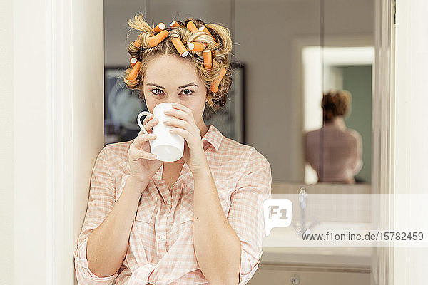Porträt einer jungen Frau mit Lockenwicklern im Haar beim Kaffeetrinken