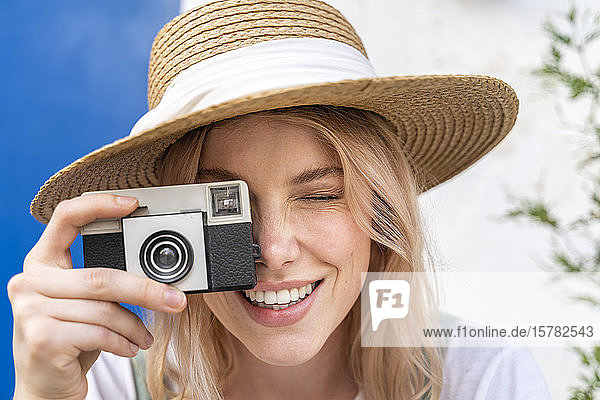 Portrait of smiling young woman wearing straw hat taking photo with camera