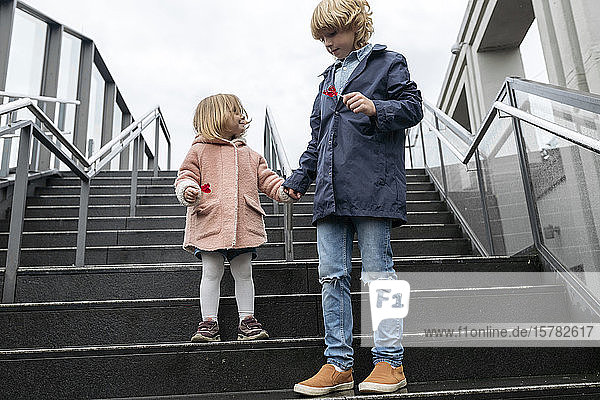 Brother and sister with lollipops standing on stairs on a rainy day